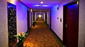 A hotel hallway with a carpeted floor, doors on both sides, and a plant on the left. - GreenTree Inn Nantong Tongzhou District Government  East Bihua Road Business Hotel (Nantong)