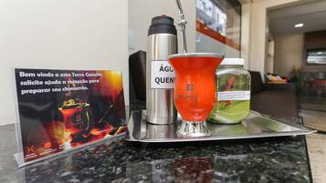 A tray with a thermos, a glass of a green drink, and a poster on a hotel counter.