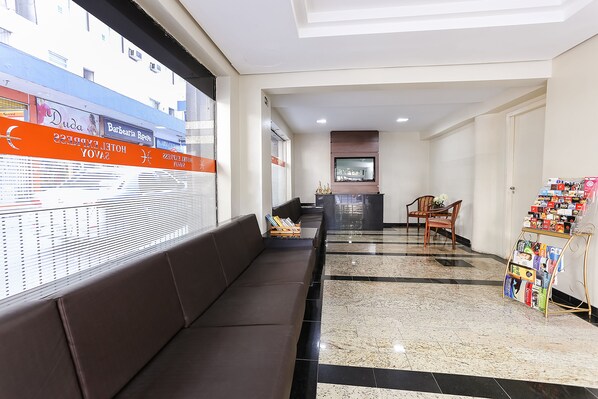 Um saguão de hotel com um balcão de recepção, um sofá marrom e um suporte para revistas.