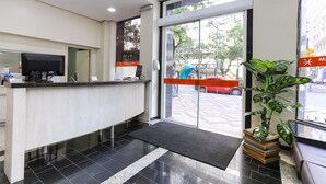 A reception area with a reception desk, a large glass door leading outside, and a potted plant.