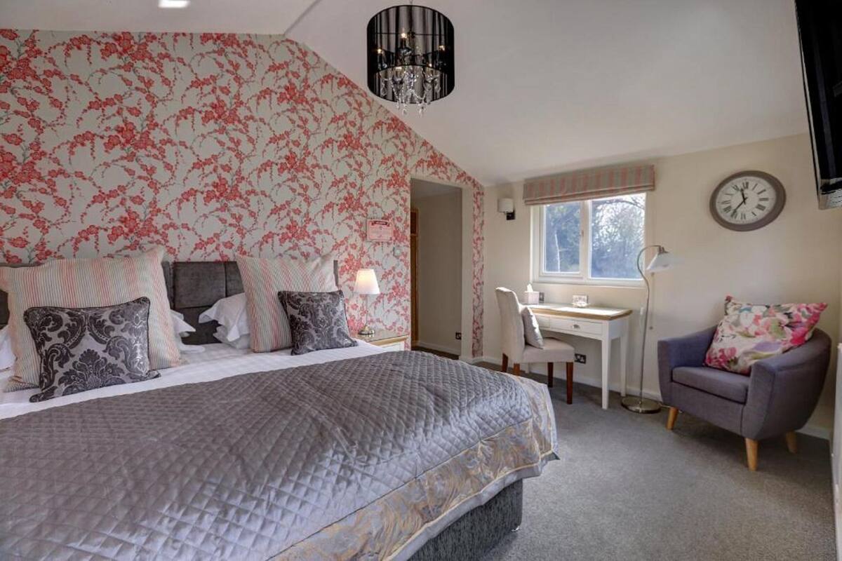 A bedroom with a bed, a desk, a chair, and a clock on the wall.