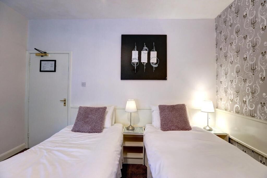 A hotel room with two single beds, a small desk, a lamp, and a framed picture on the wall.