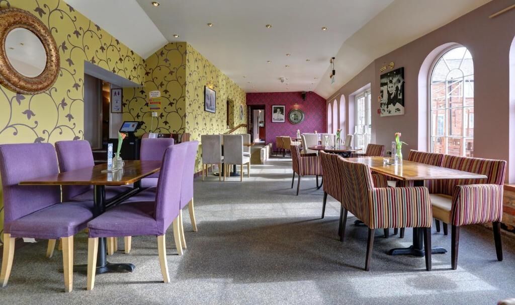 A hotel dining area with purple and striped seating, a central table, and patterned wallpaper.