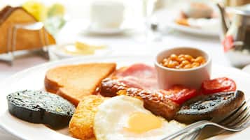Une assiette de petit-déjeuner comprenant des toasts, des œufs, des saucisses, des tomates, des haricots et un champignon grillé.