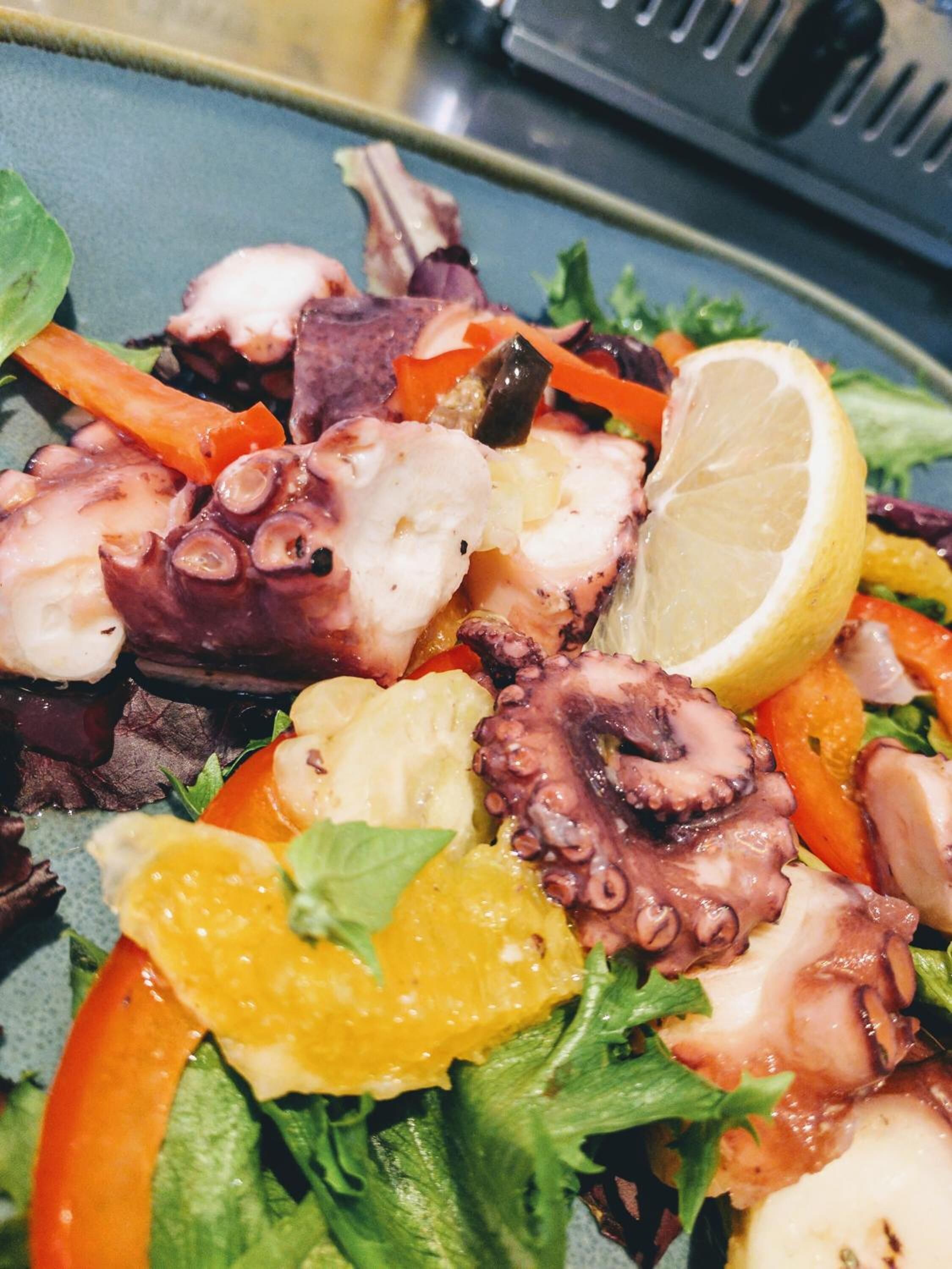 A plate of grilled octopus with vegetables and a lemon wedge.