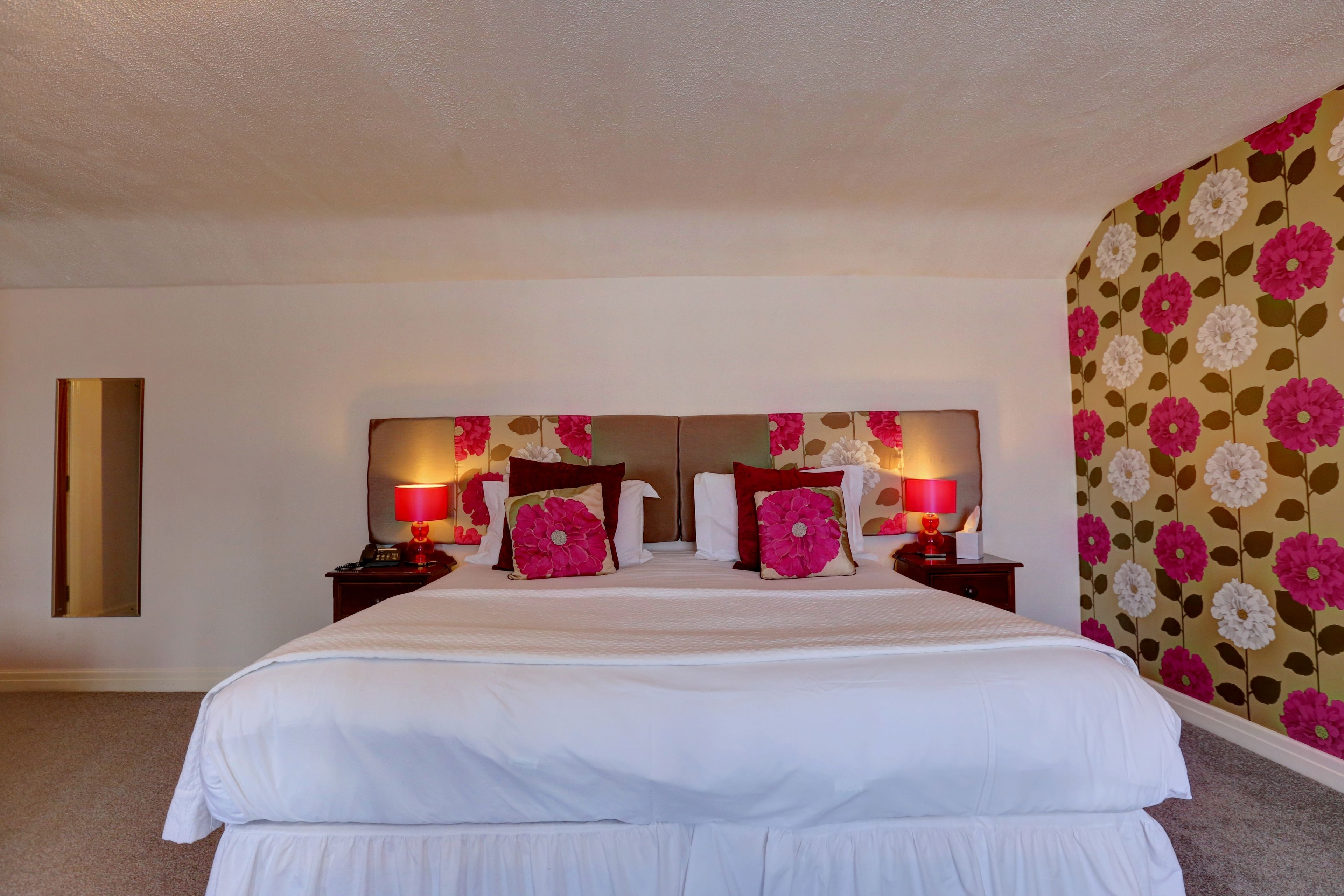 A hotel room with a large bed, two bedside tables with lamps, and a floral wallpaper on one wall.