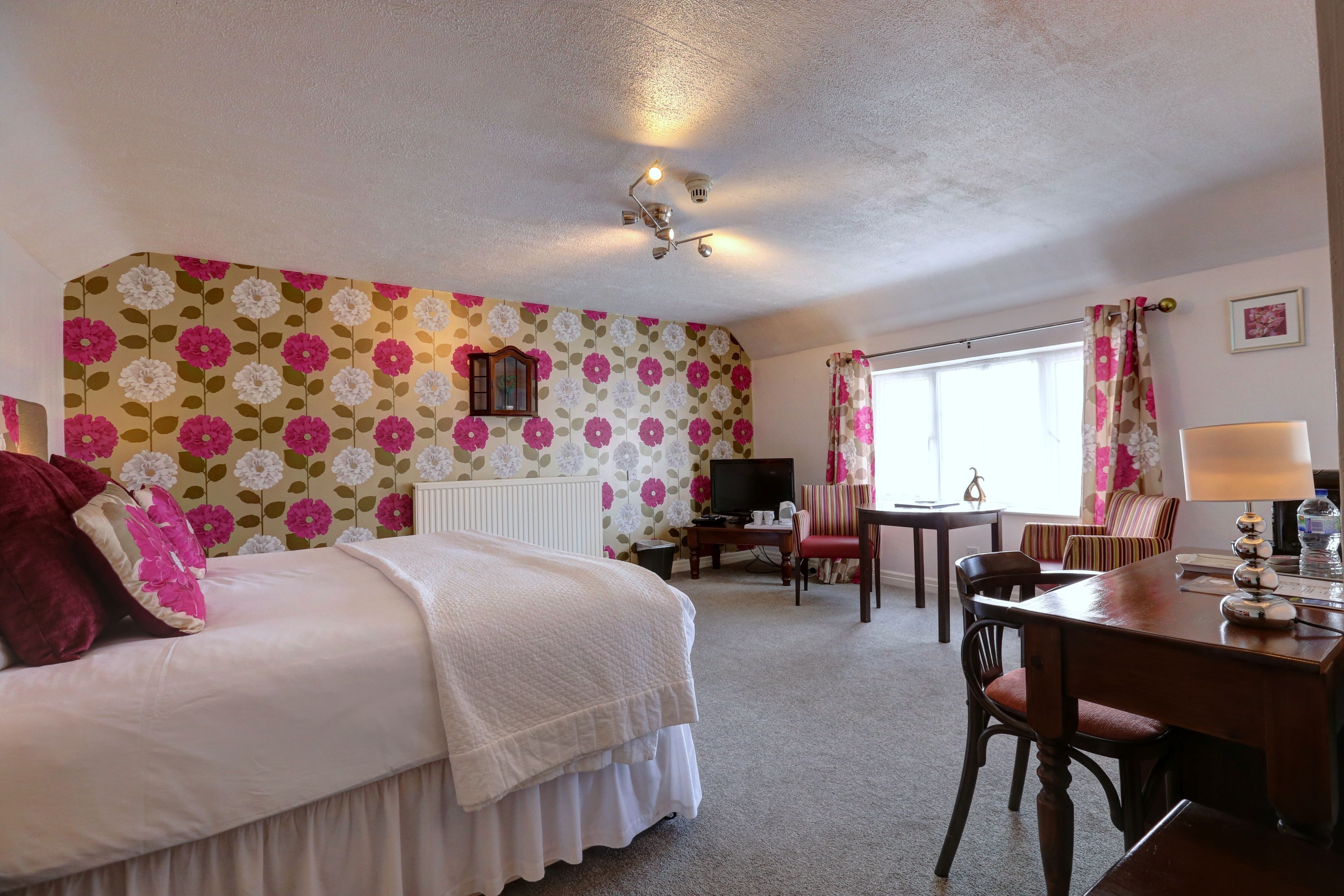 Habitación de hotel con cama, escritorio, silla, televisor y ventana con cortinas.
