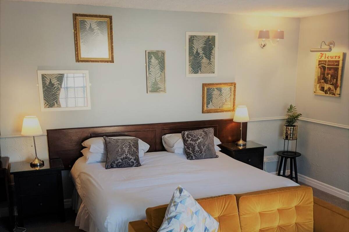 A hotel room with a large bed, two bedside tables with lamps, a sofa, and wall art.