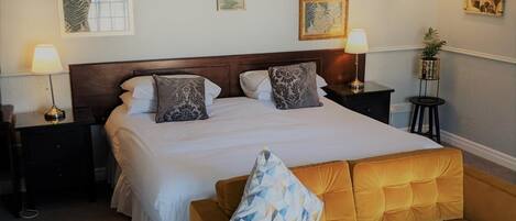 A hotel room with a large bed, two bedside tables with lamps, a sofa, and wall art.