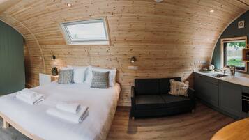 A cozy, wooden cabin-style room with a bed, a sofa, a small kitchen area, and a window.