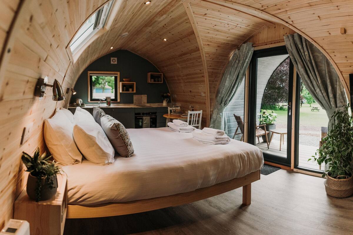 A cozy bedroom with a large bed, a wooden headboard, and a view of a dining area through a glass door.