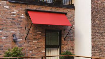 A two-story building with a red awning, brick walls, and a balcony with plants.