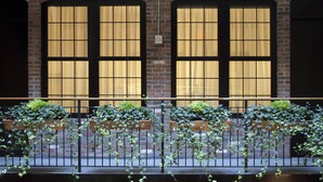 A building facade with large windows, brick arches, and a metal railing with greenery. - The Broome (New York)