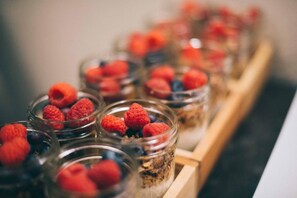 A series of glass jars containing raspberries and blueberries, arranged on a wooden tray. - The Broome (New York)