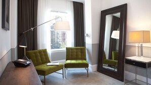 A hotel room with a green armchair, a desk with a lamp, and a large mirror. - The Broome (New York)