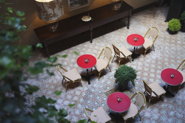 Una terraza con suelo estampado, sillas de mimbre y mesas de color rojo.