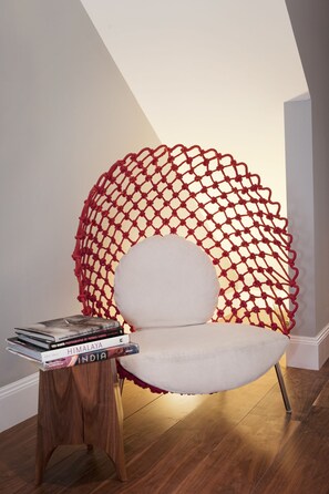 A chair with a red netted backrest and a stack of books on a wooden side table. - The Broome (New York)