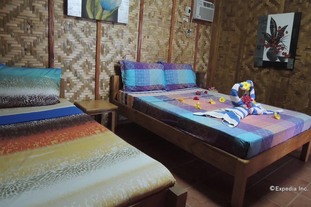A room with two wooden beds, a woven wall, and a painting of flowers.