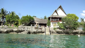 A beachfront property with a thatched-roof structure, a white building with a balcony, and clear turquoise water. - Asian Belgian Resort (Moalboal)