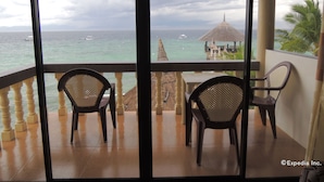 A balcony with two chairs, a table, and a view of the ocean with boats and a thatched structure. - Asian Belgian Resort (Moalboal)