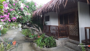 A traditional thatched-roof house with a small porch, surrounded by lush greenery and flowering plants. - Asian Belgian Resort (Moalboal)