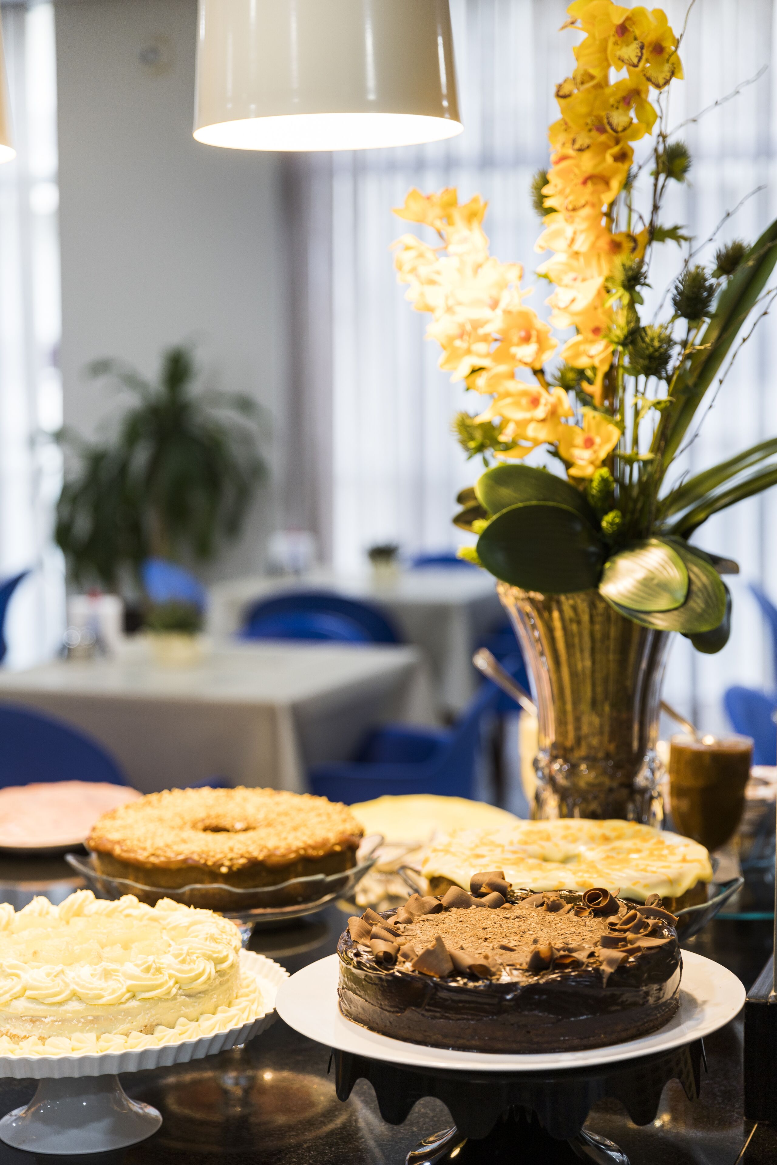 A table with various cakes and a vase of yellow flowers.
