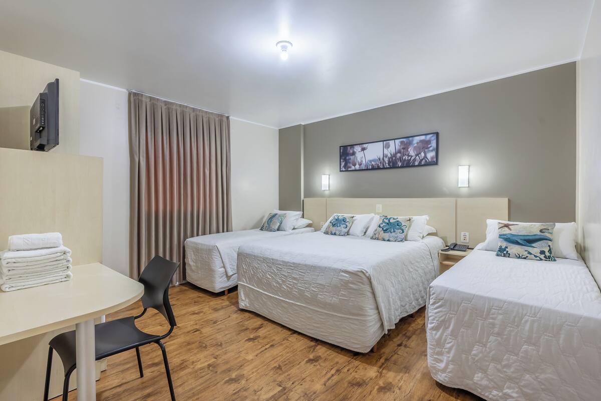 A hotel room with two beds, a desk, a chair, a flat-screen TV, and a painting on the wall.