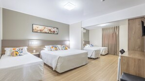 Ein Hotelzimmer mit drei Betten, einem Flachbildfernseher, einem Gemälde an der Wand und einem Holzboden.