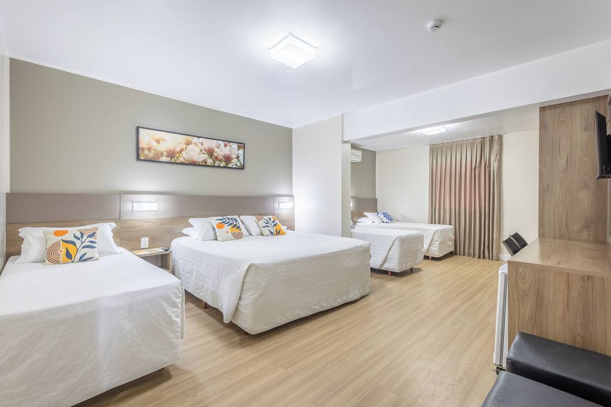 A hotel room with three beds, a flat-screen TV, a painting on the wall, and a wooden floor.