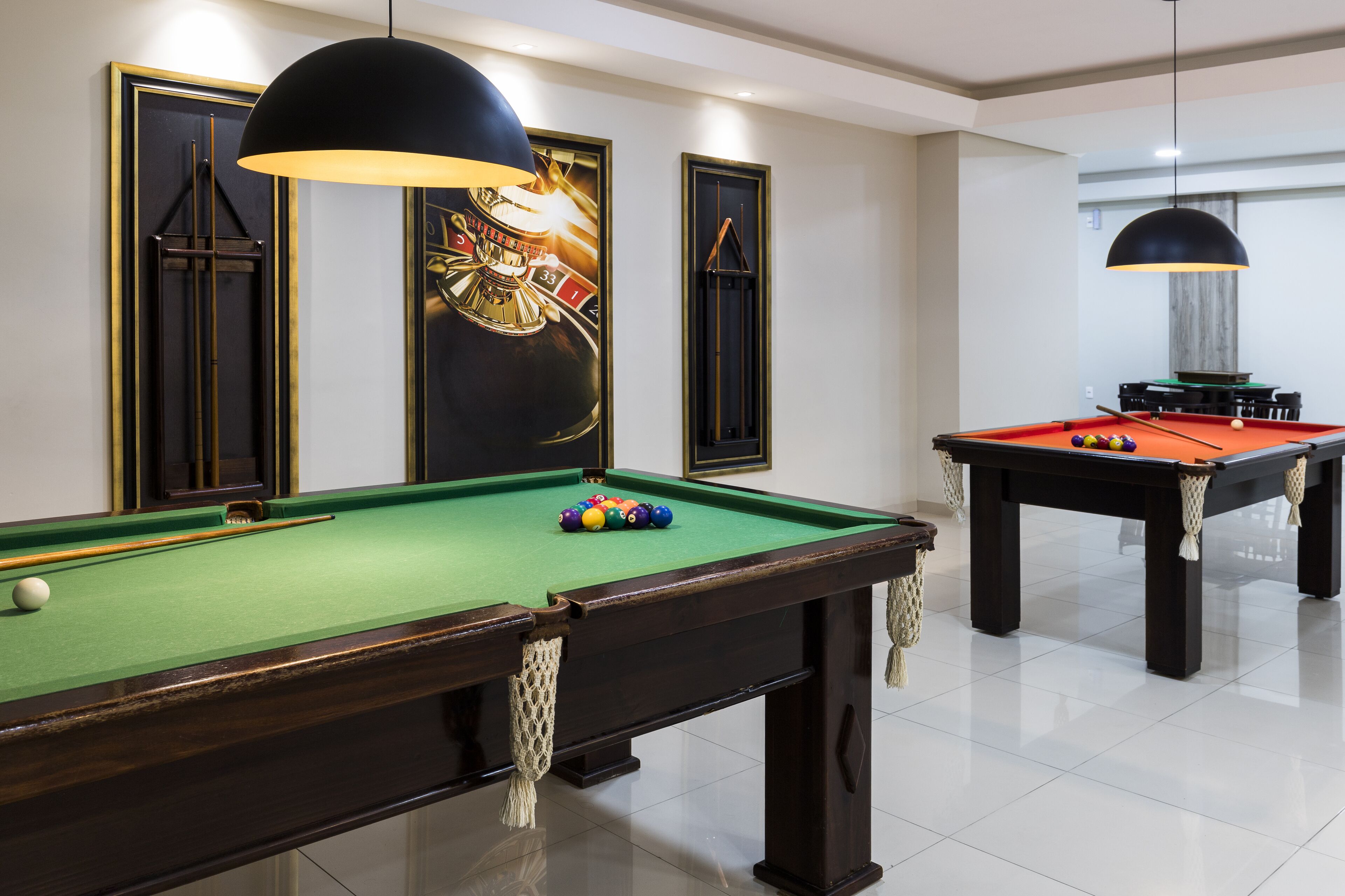 A pool table with balls, a second table in the background, and a large decorative mirror with a golden frame.