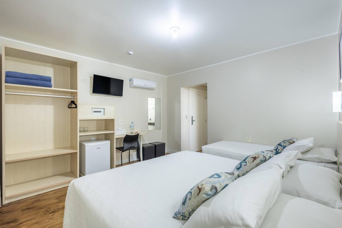 A hotel room with a bed, a desk with a chair, a TV, and a wardrobe.