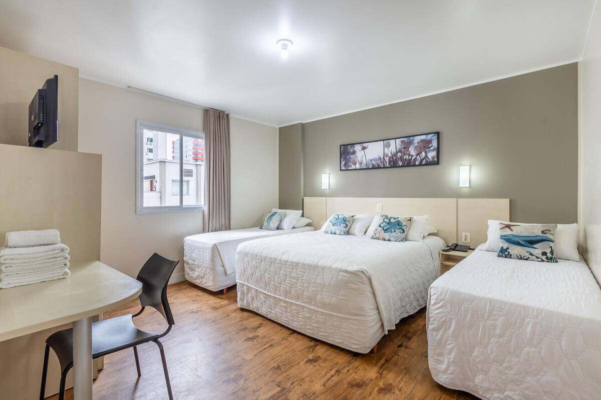 A hotel room with two beds, a desk, a chair, a window with curtains, a painting on the wall, and a ceiling light.