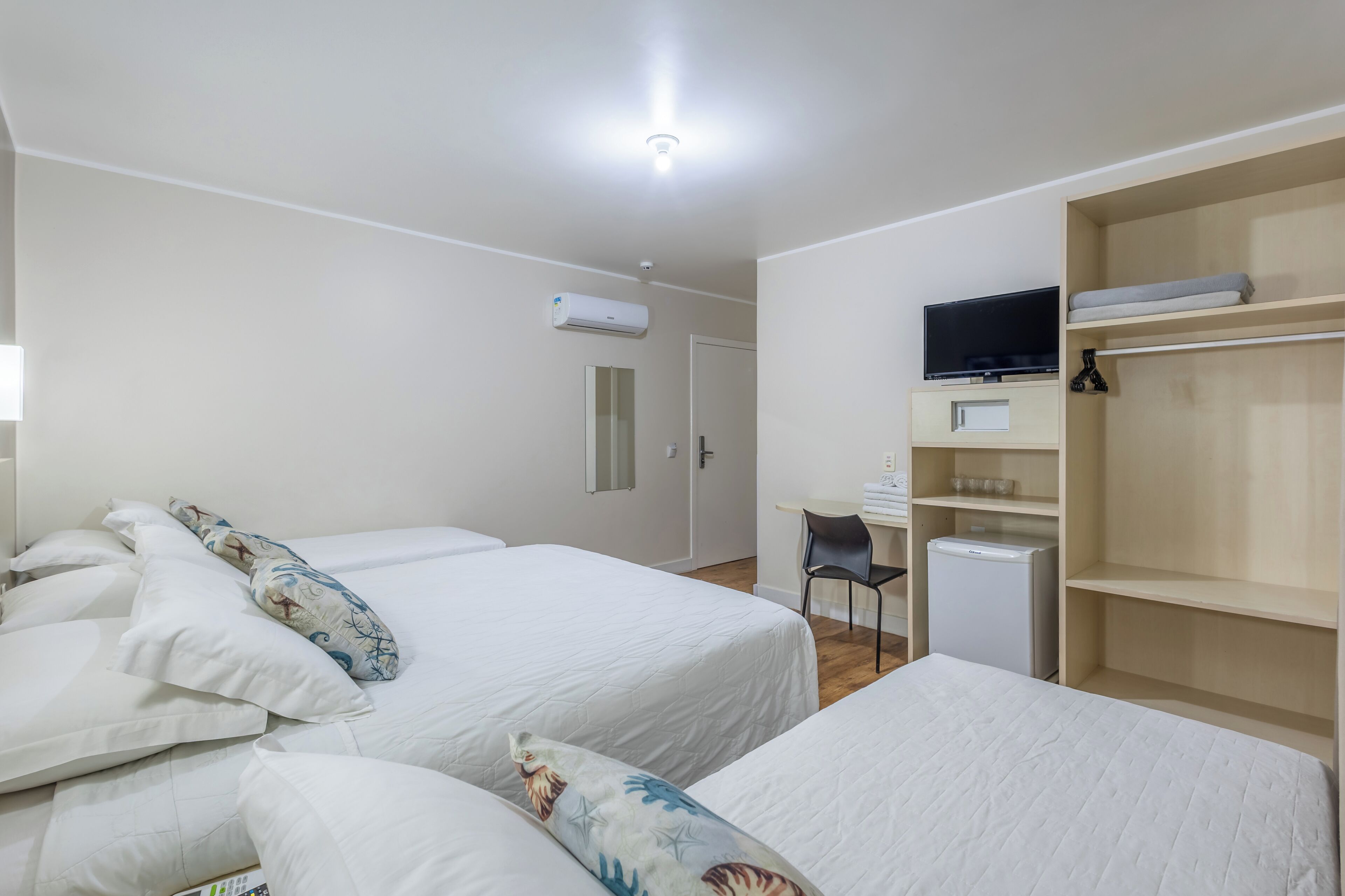 Ein Hotelzimmer mit zwei Betten, einem Schreibtisch, einem Stuhl, einem Fernseher und einem Kleiderschrank.