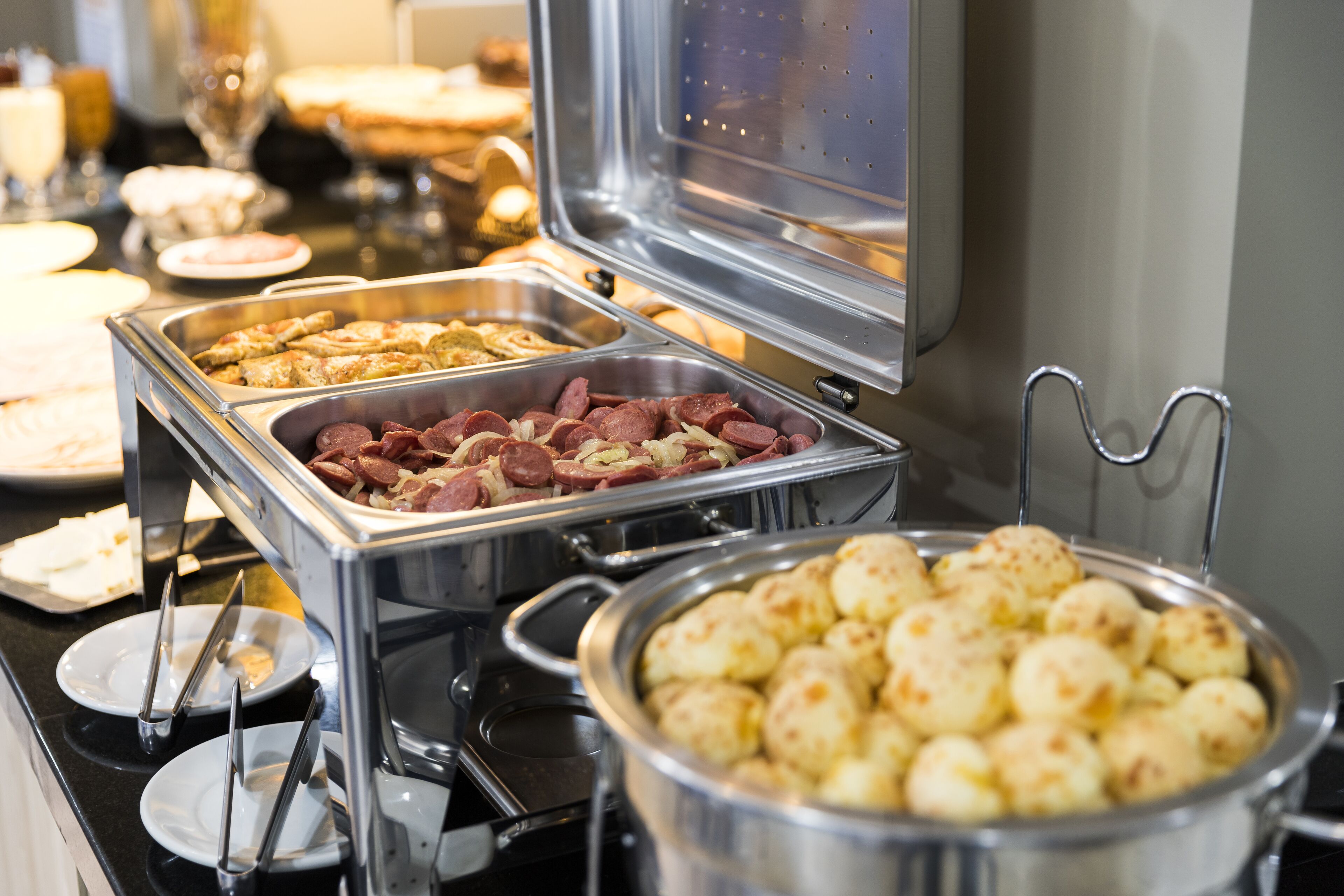 Een buffet met diverse gerechtjes, waaronder worstjes, gebak en een grote pan gekookte aardappelen.