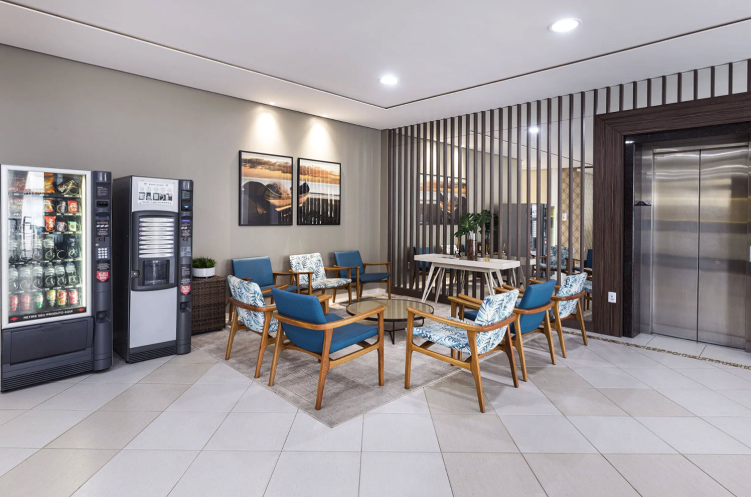 A modern indoor space with vending machines, a dining area with blue chairs, and an elevator.