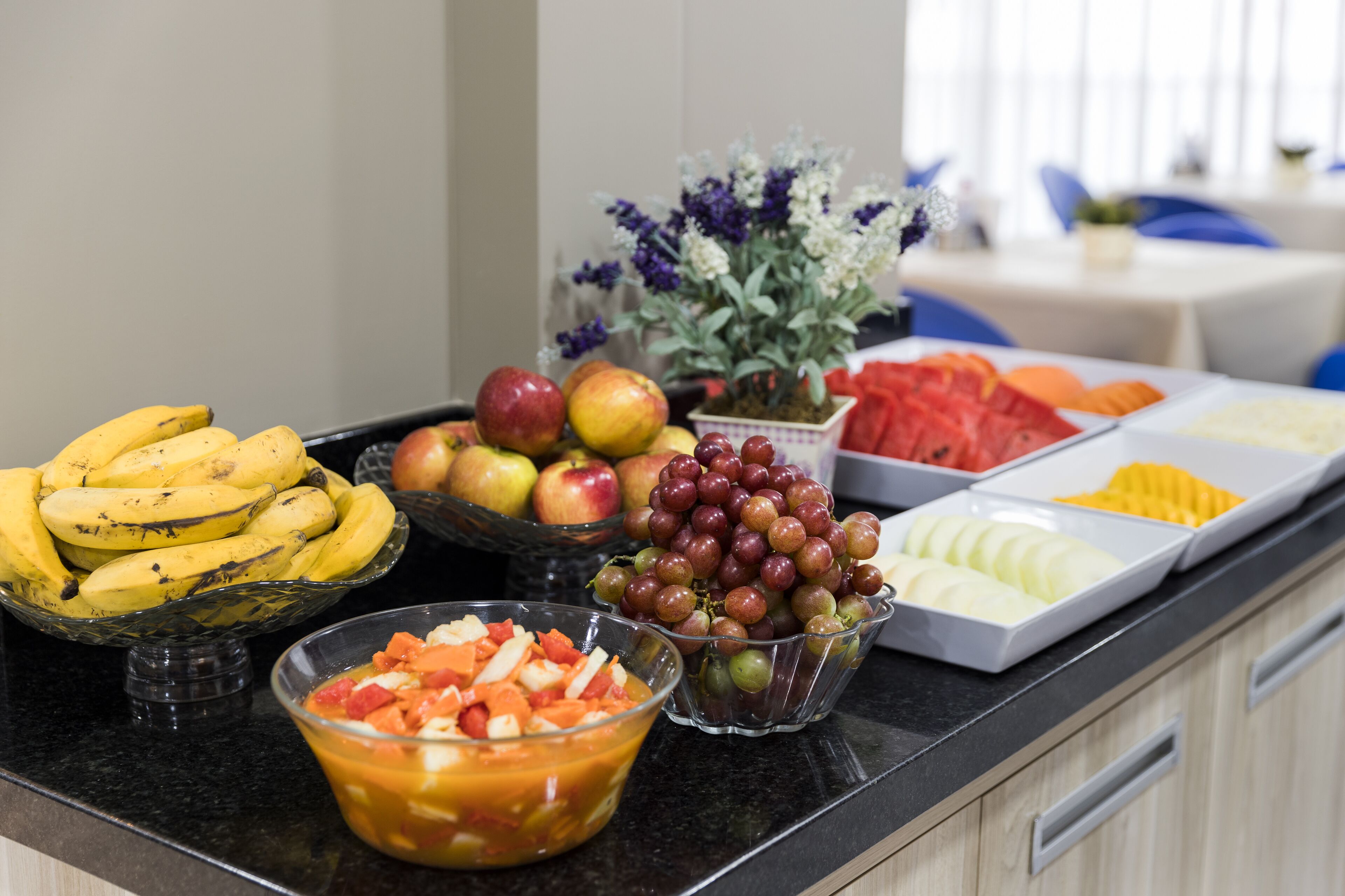 Buffet de café da manhã com frutas variadas e um arranjo de flores.