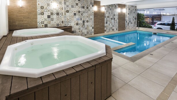 Ein Swimmingpool mit zwei Whirlpools, gefliesten Wänden und einer Holzterrasse.