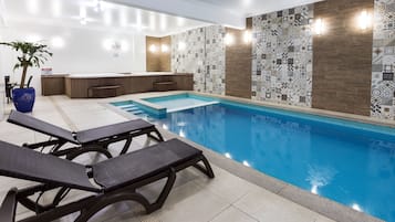 A swimming pool with lounge chairs, a hot tub, and patterned walls.
