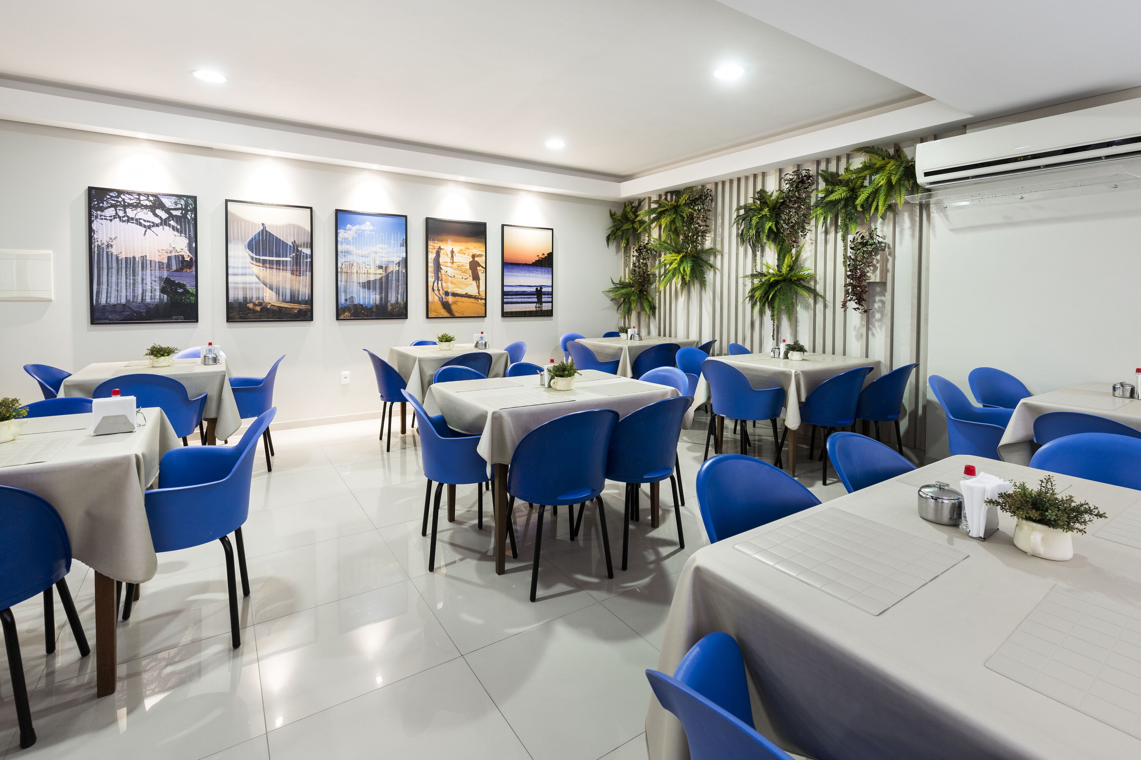 Een moderne eetruimte met blauwe stoelen en tafels, met kunstwerken aan de muur en potplanten.