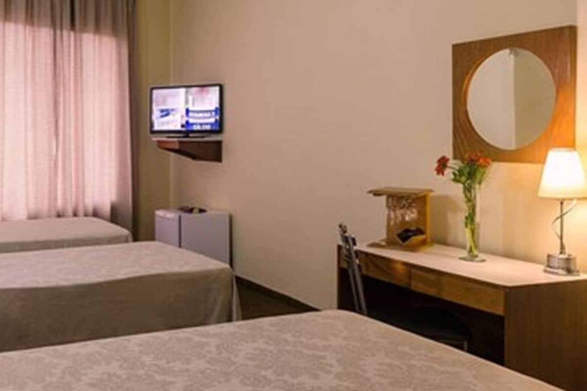 Habitación de hotel con dos camas, televisión, escritorio con lámpara y espejo.