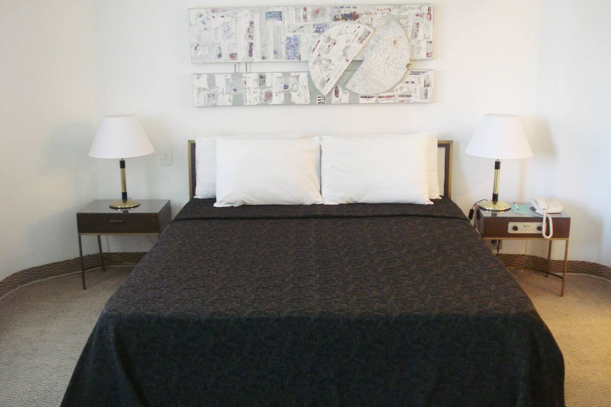 Habitación de hotel con una cama grande, dos mesitas de noche con lámparas, una obra de arte con un mapa en la pared y piso cubierto de alfombra.