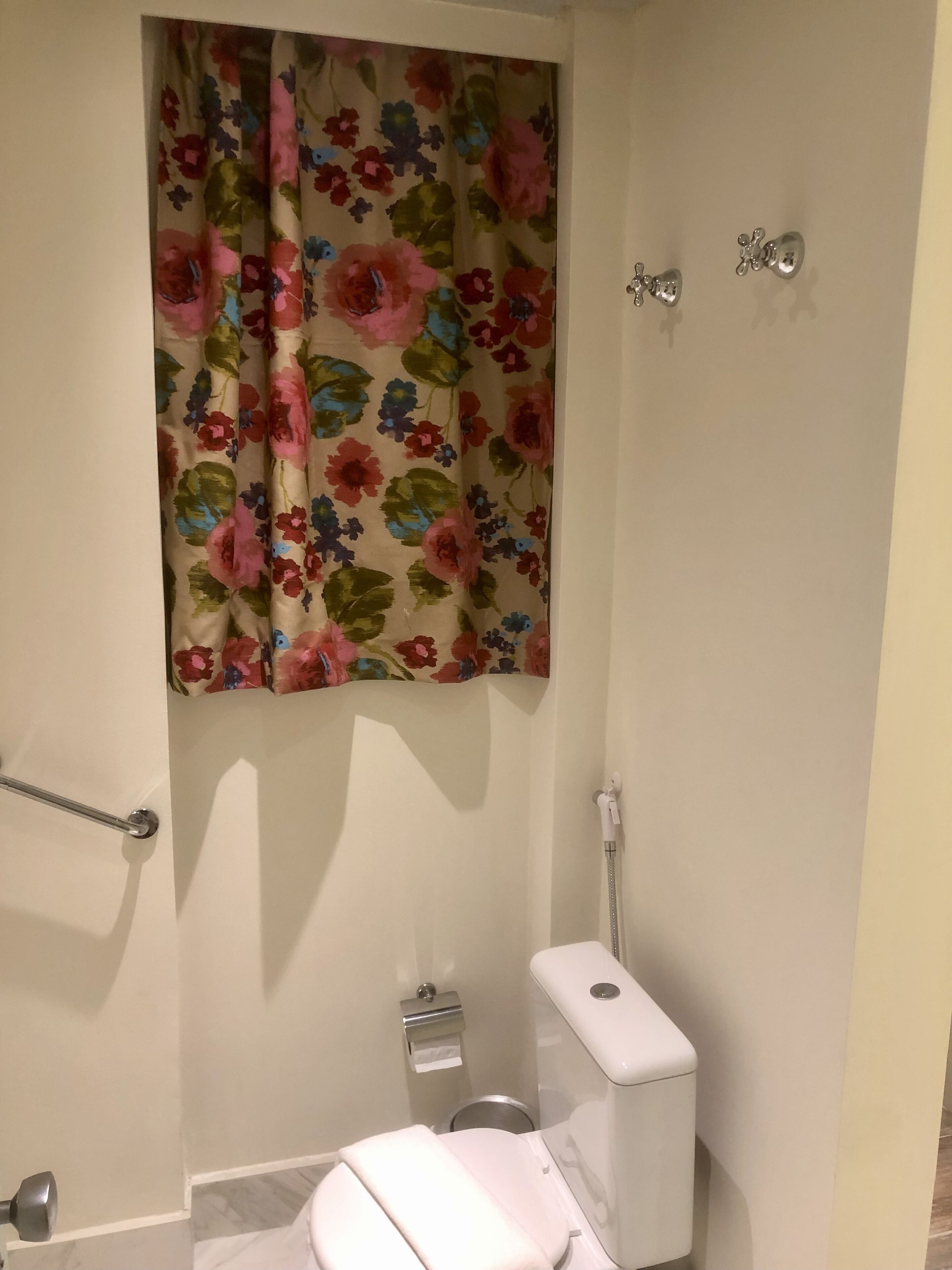 A bathroom with a toilet, a shower, and a floral curtain.