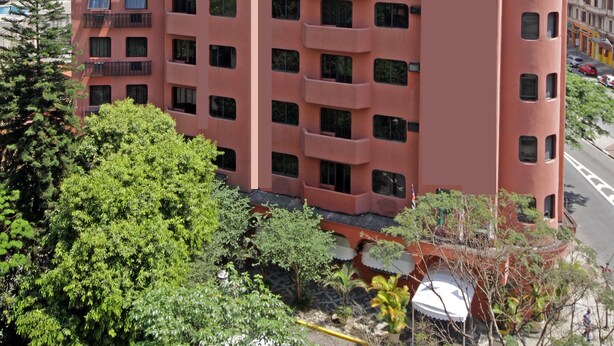 Un hotel de varios pisos con una fachada rosa distintiva, llamado 'San Michel Hotel'. Presenta un diseño arquitectónico moderno con balcones en los pisos superiores.
