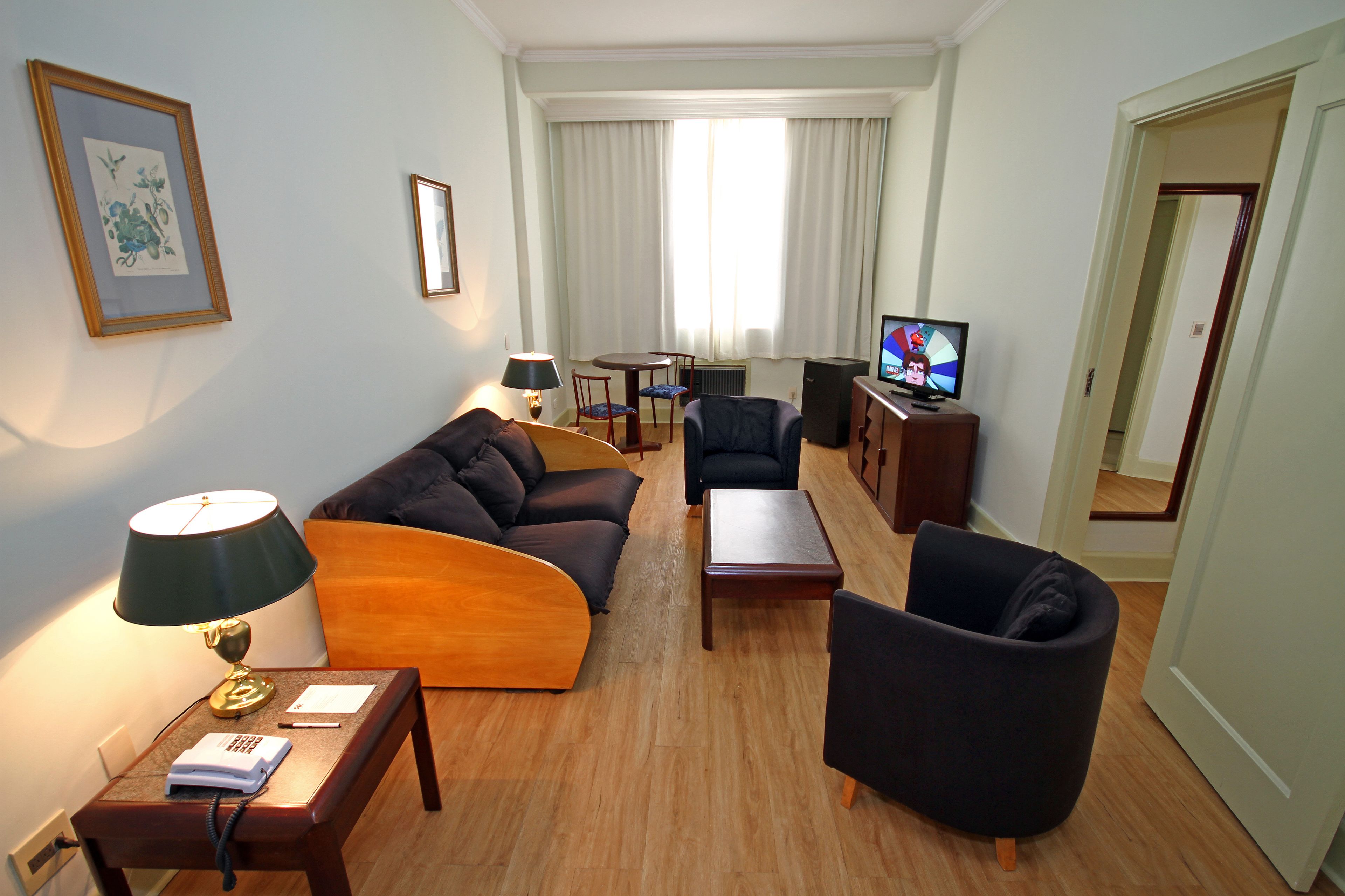 Una habitación de hotel moderna con sofá, sillón, una mesita, televisor y lámpara.