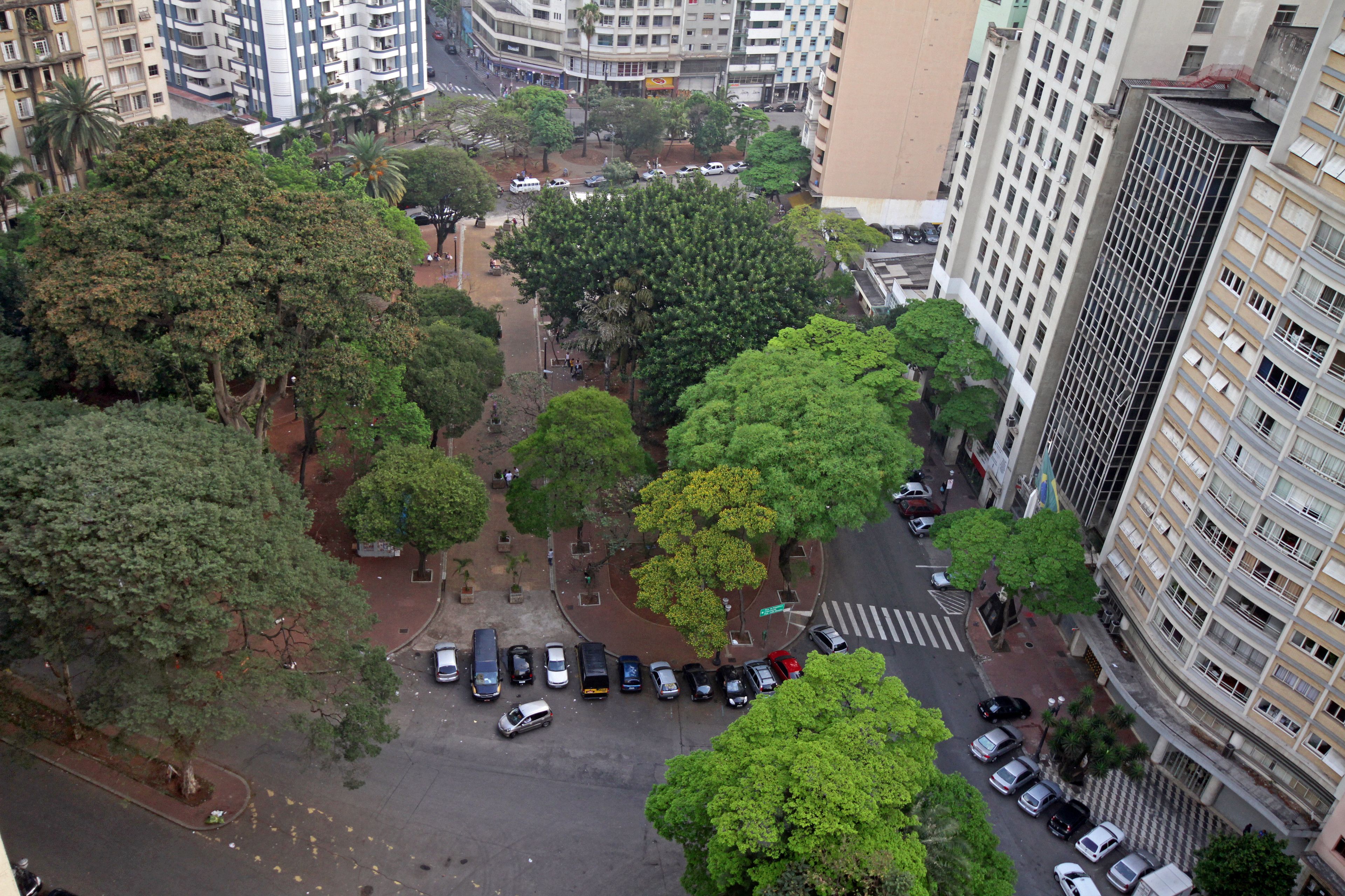 Une vue aérienne d’une ville avec de hauts immeubles, un parc central avec des arbres et un parking rempli de voitures.