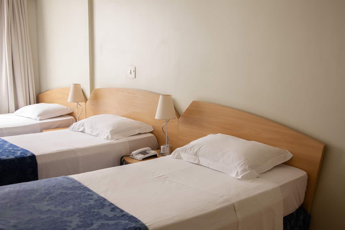 Une chambre d’hôtel avec deux lits simples, chacun étant équipé d’une table de chevet, d’une lampe et d’un téléphone.