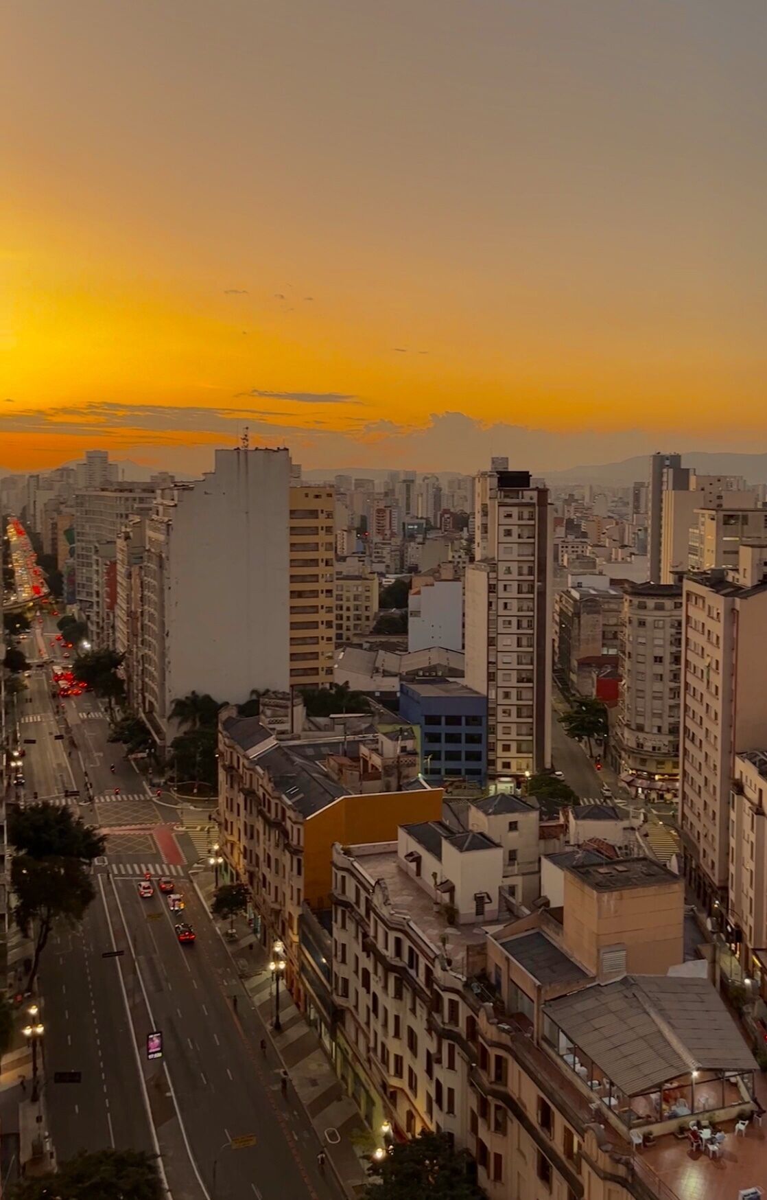 A cityscape at sunset with high-rise buildings, a busy street, and a clear sky.
