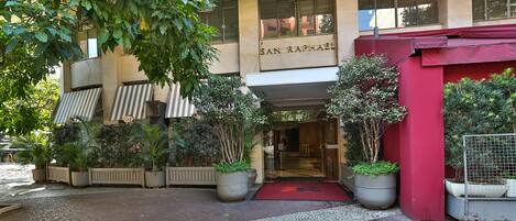 A hotel entrance with a red awning, potted plants, and a tiled walkway.