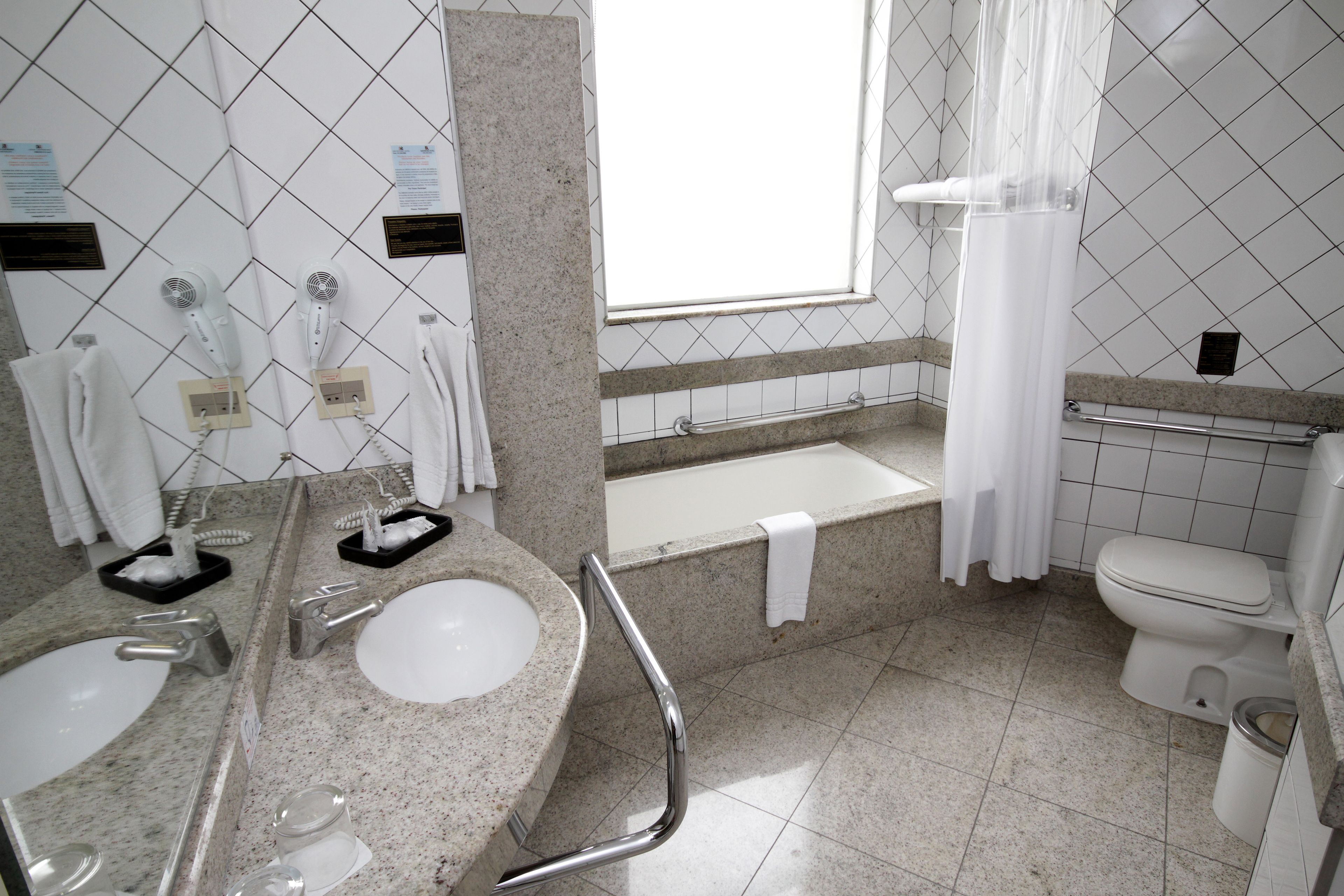 Uma casa de banho com duas pias, uma banheira, uma sanita e uma janela com cortina.