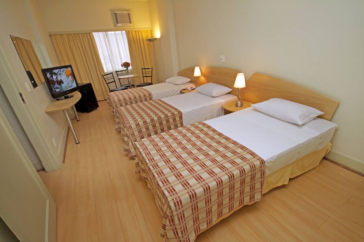 Une chambre d’hôtel avec trois lits, une télévision, un bureau et une chaise.